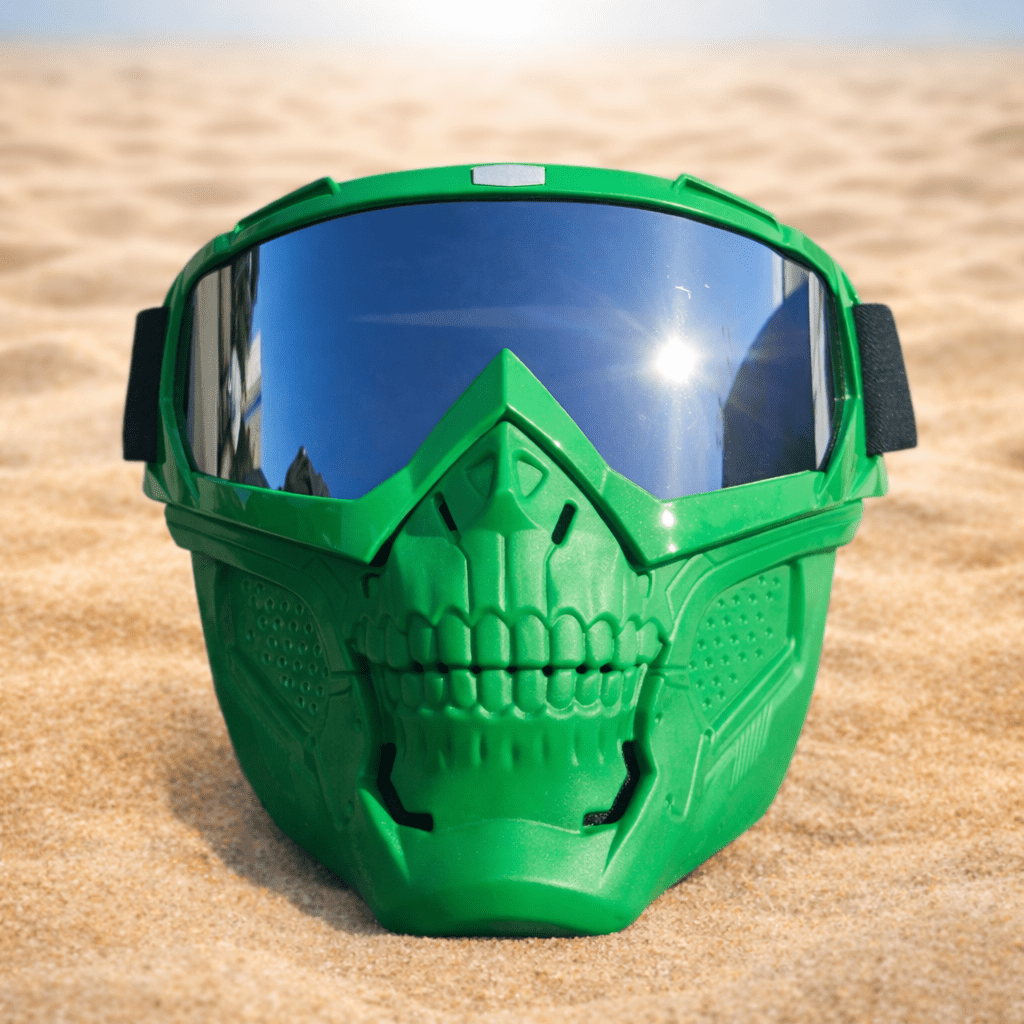 Green Skelet Silver Goggles Mask on a sandy surface with a bright sun, showcasing its aggressive design and futuristic goggles.